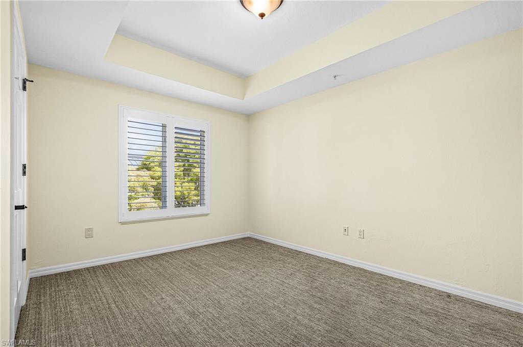 Room featuring a tray ceiling, plantation shutters, and textured carpeting