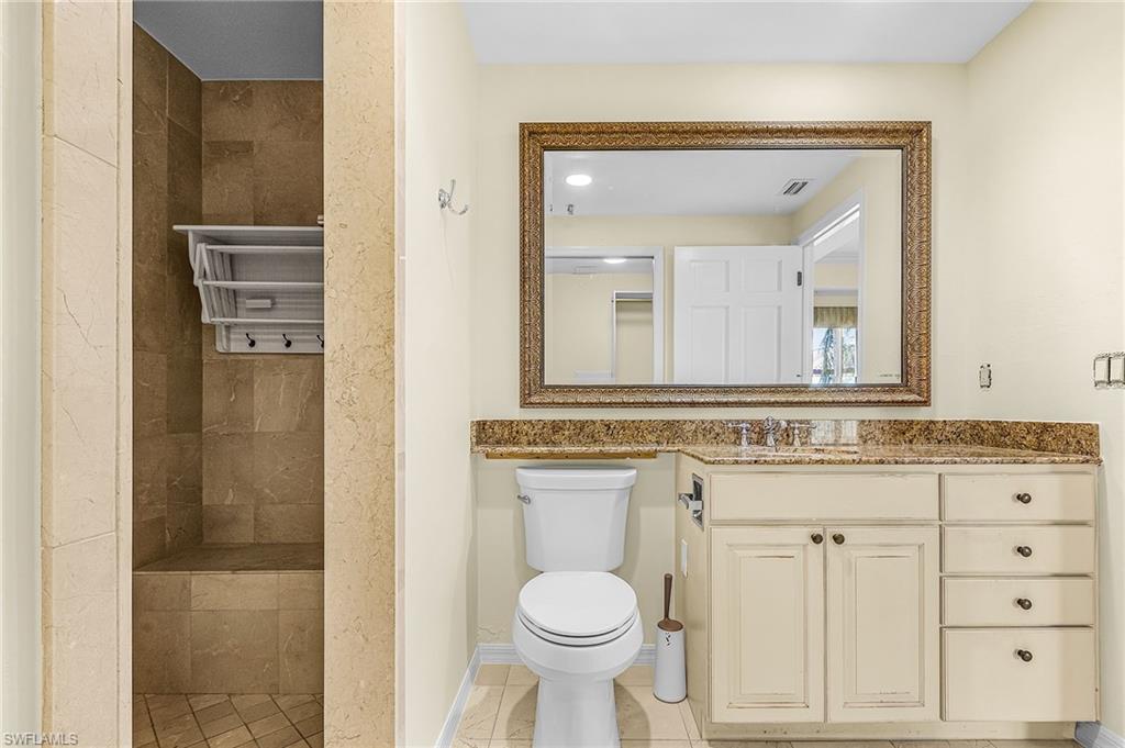 Bathroom featuring a walk-in shower with tiled walls and a built-in bench, a vanity with a stone countertop, an undermount sink, and cabinet storage, a large framed mirror, and light-colored walls