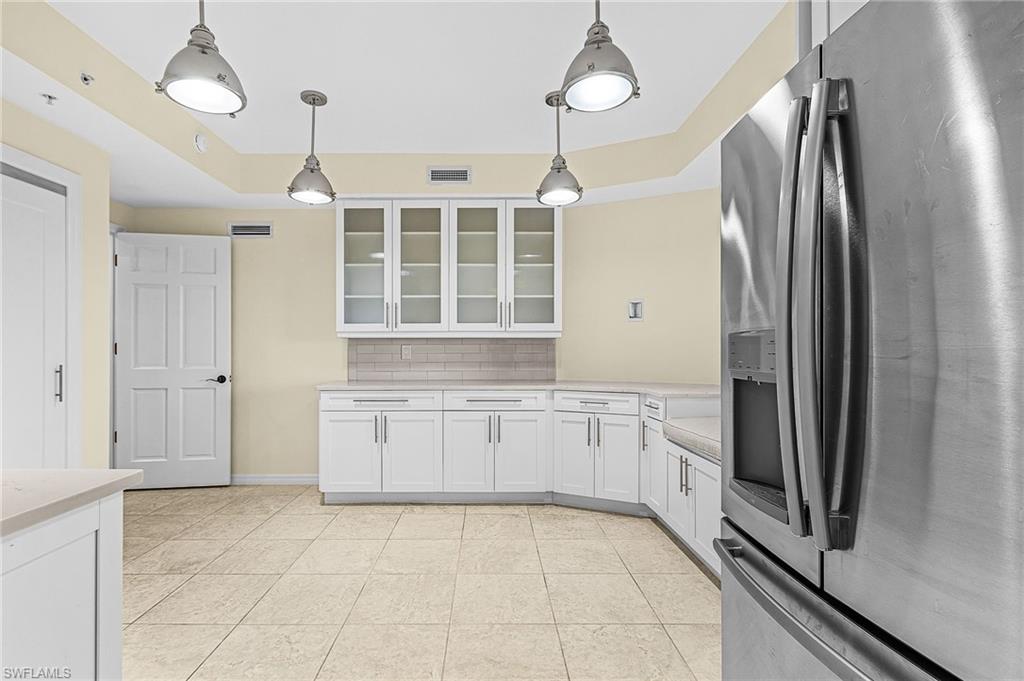 Stainless steel refrigerator featured in a kitchen with white cabinetry, light-toned countertops, and a subway tile backsplash