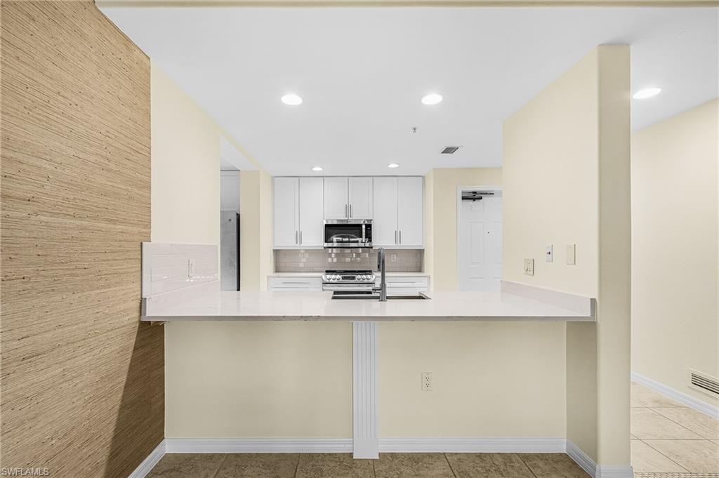 Modern kitchen featuring white cabinetry, stainless steel appliances, a white tile backsplash, and a large countertop with an integrated sink