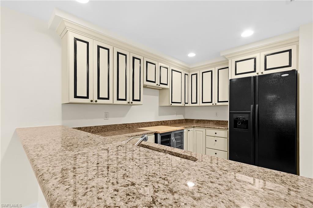 Kitchenette featuring extensive light-toned cabinetry with dark trim, complementing granite countertops, and a full-size black refrigerator