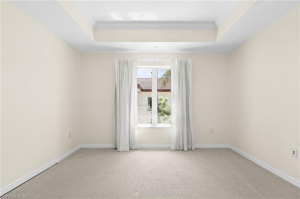 Recessed ceiling with layered trim, framed window with white curtains, light-toned carpet flooring, neutral wall paint, and white baseboards