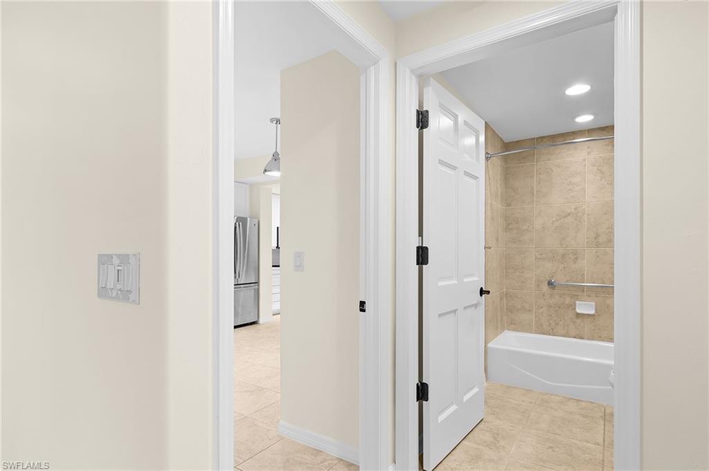 Bathroom featuring a white tub, light-toned tiled shower surround, recessed lighting, and a grab bar