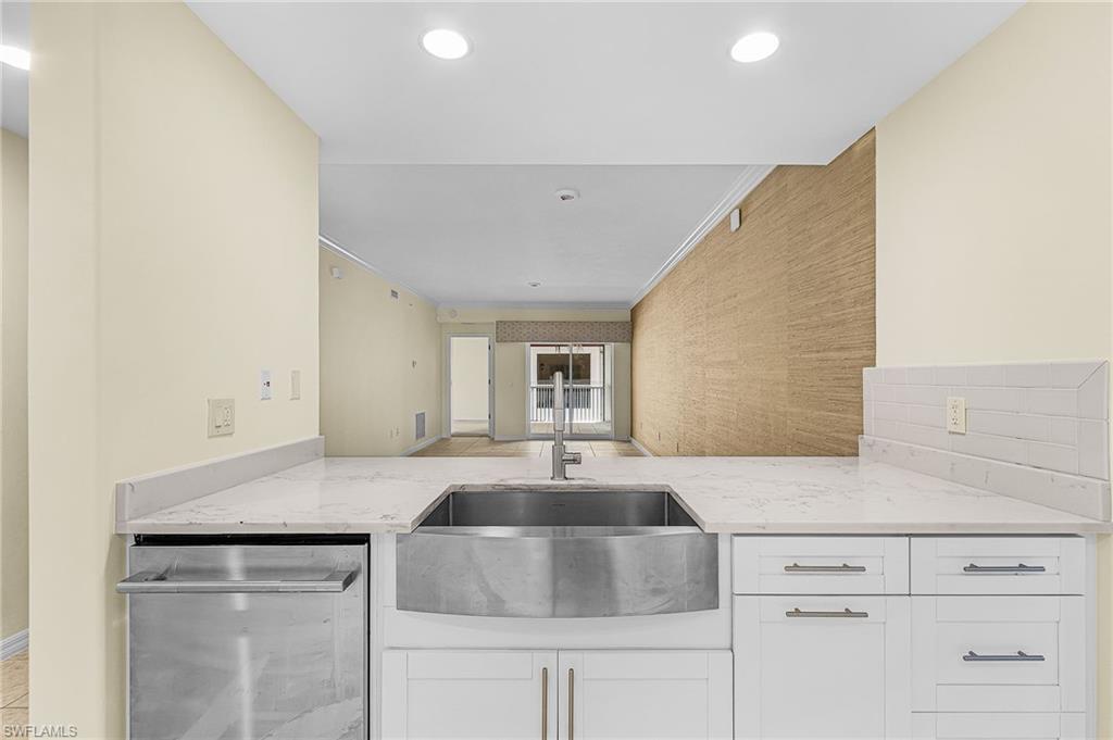 Kitchen featuring a stainless steel farmhouse sink, white shaker cabinetry, light-toned countertops, and a subway tile backsplash