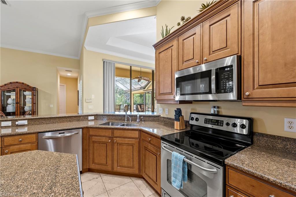 Kitchen featuring appliances with stainless steel finishes, a sink, brown cabinetry, a tray ceiling, and ornamental molding