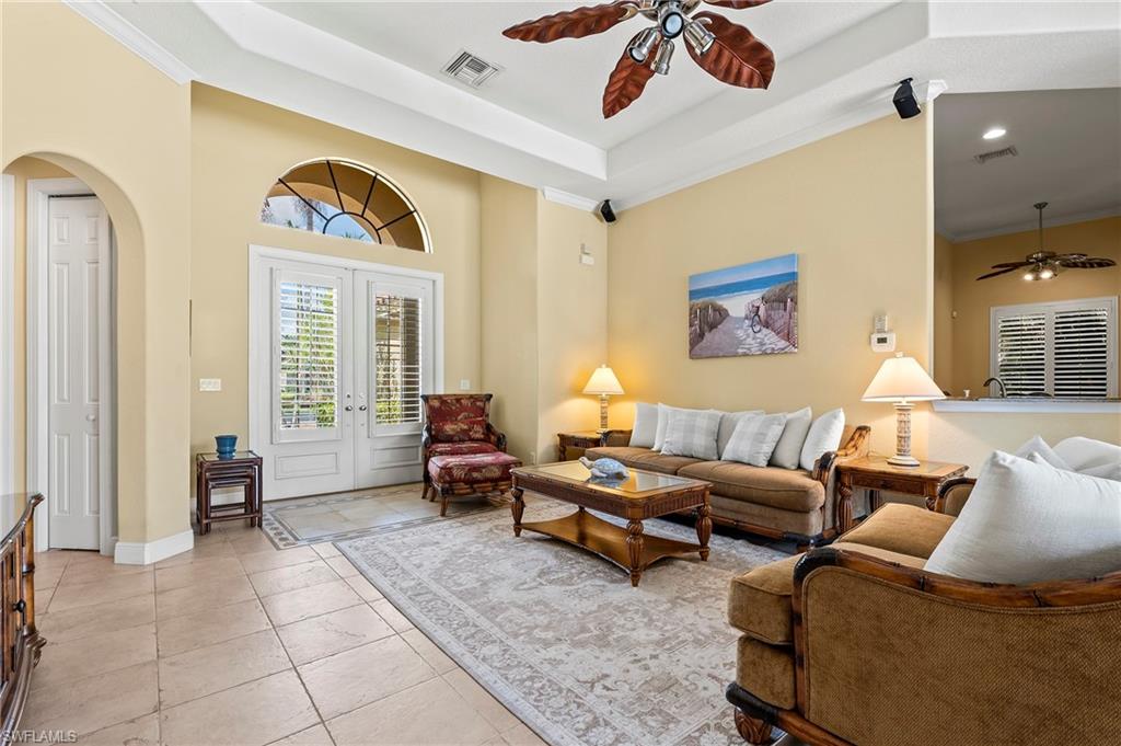 Living room featuring a ceiling fan, arched walkways, light tile patterned floors, french doors, and baseboards