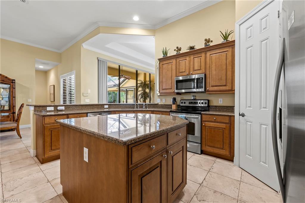 Kitchen featuring appliances with stainless steel finishes, a peninsula, brown cabinetry, a center island, and crown molding