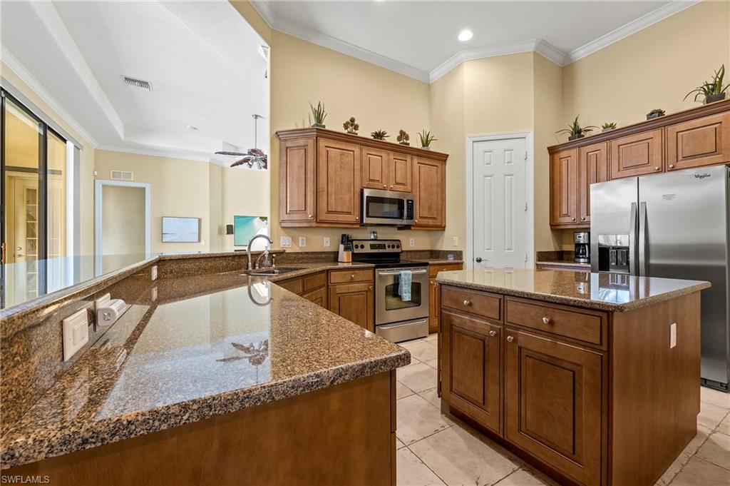 Kitchen featuring stainless steel appliances, a center island, brown cabinets, dark stone counters, and a peninsula