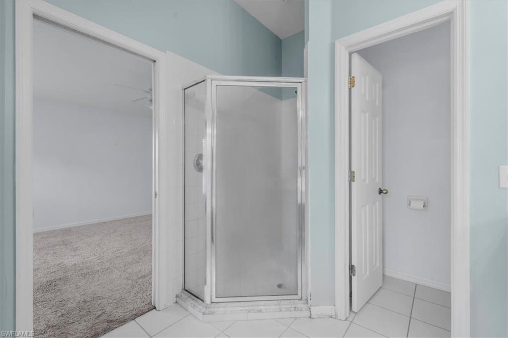 Glass-enclosed corner shower with white subway tile interior, set on a white tiled floor