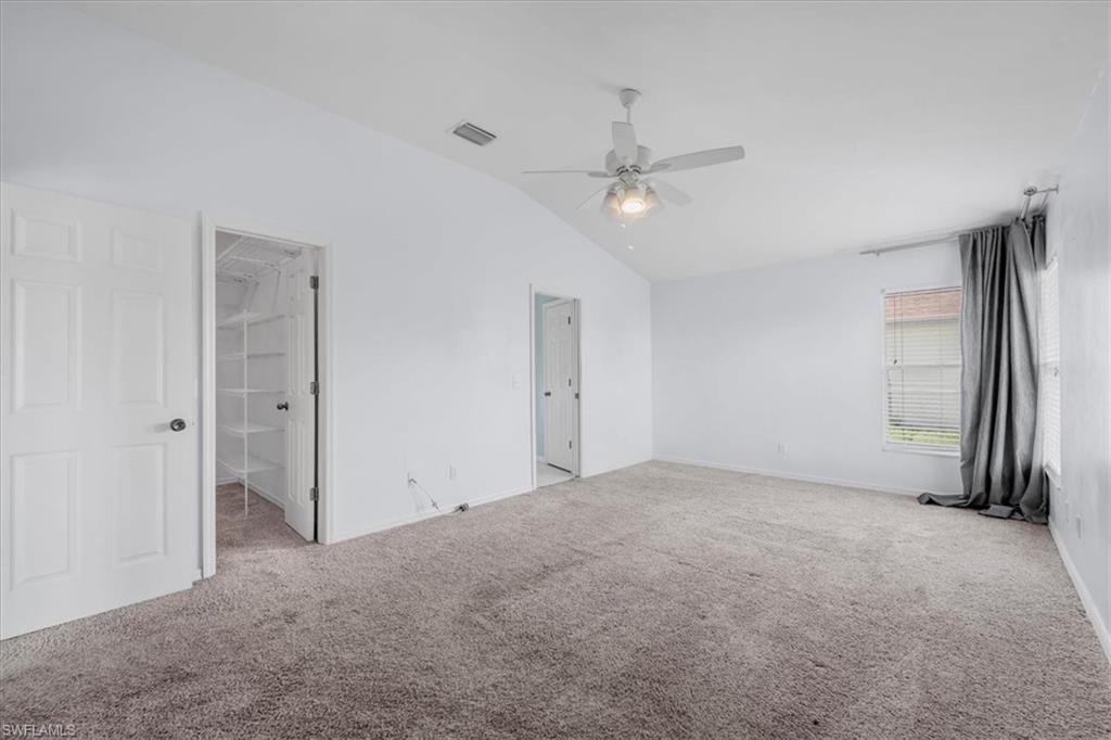 Spacious room featuring vaulted ceilings, textured carpet flooring, a ceiling fan with light fixture, and a window with horizontal blinds