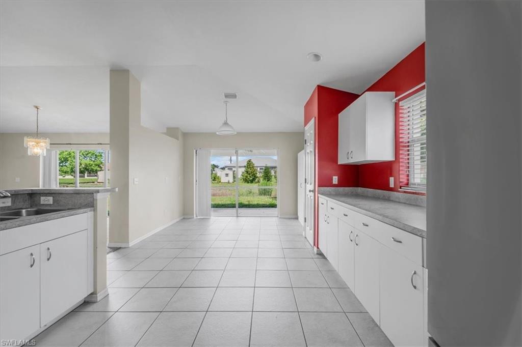 Kitchen and dining area featuring tile flooring, white cabinetry, contrasting red accent wall, and a sliding glass door leading to the exterior