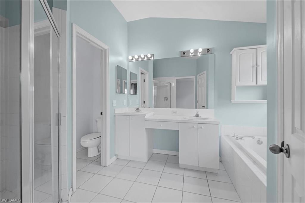 Bathroom featuring a dual vanity, built-in cabinetry, large mirror with vanity lighting, tiled flooring, and a garden tub