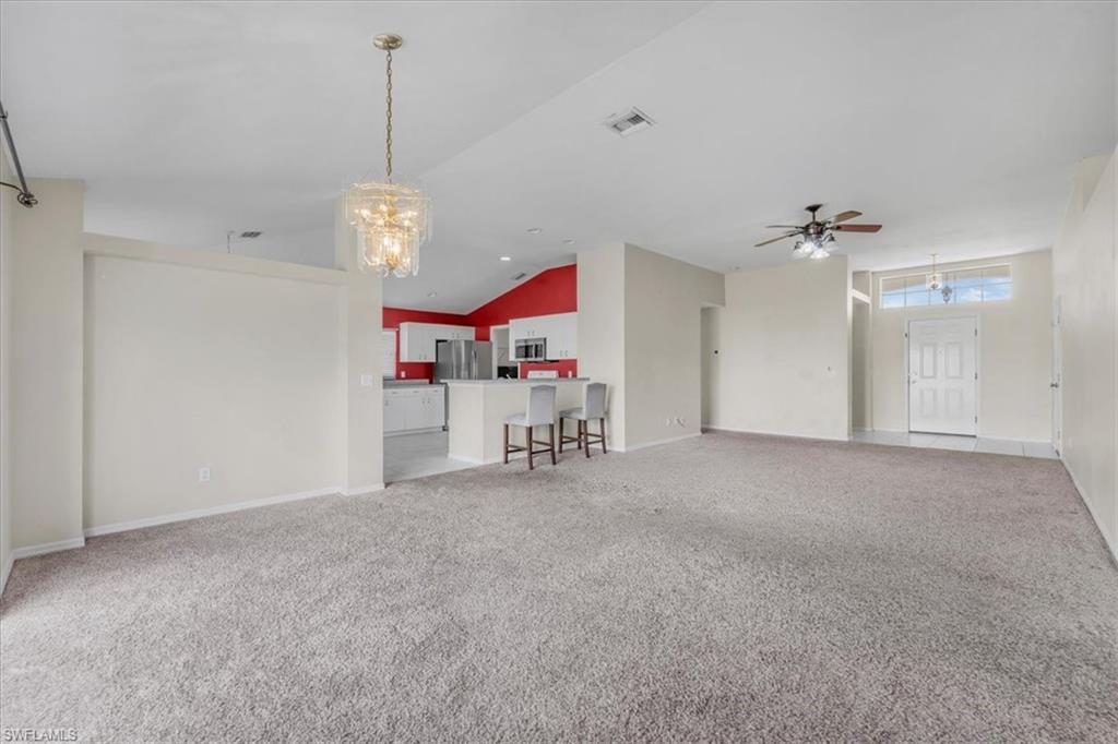 Spacious open-concept living area featuring soft gray carpeting, a contemporary chandelier, and a ceiling fan