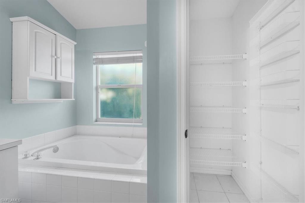 Built-in soaking tub with white tile surround, illuminated by a window with blinds