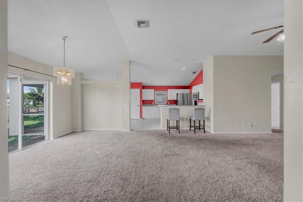 Open-concept living space featuring neutral carpet flooring, a contemporary chandelier, and sliding glass doors