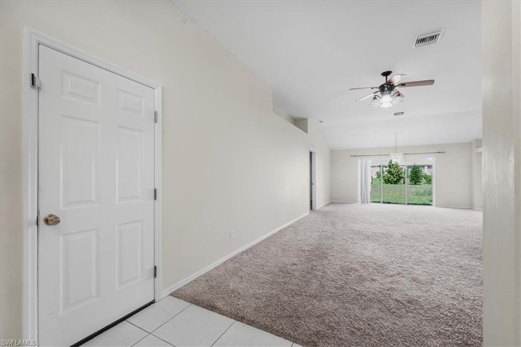 Spacious living area featuring neutral carpeting, a ceiling fan with integrated lighting, and vaulted ceilings
