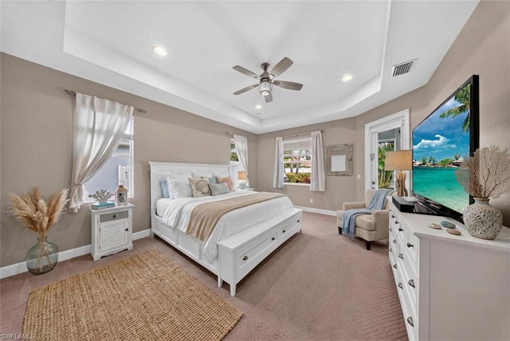 Spacious bedroom featuring a tray ceiling with recessed lighting and a ceiling fan