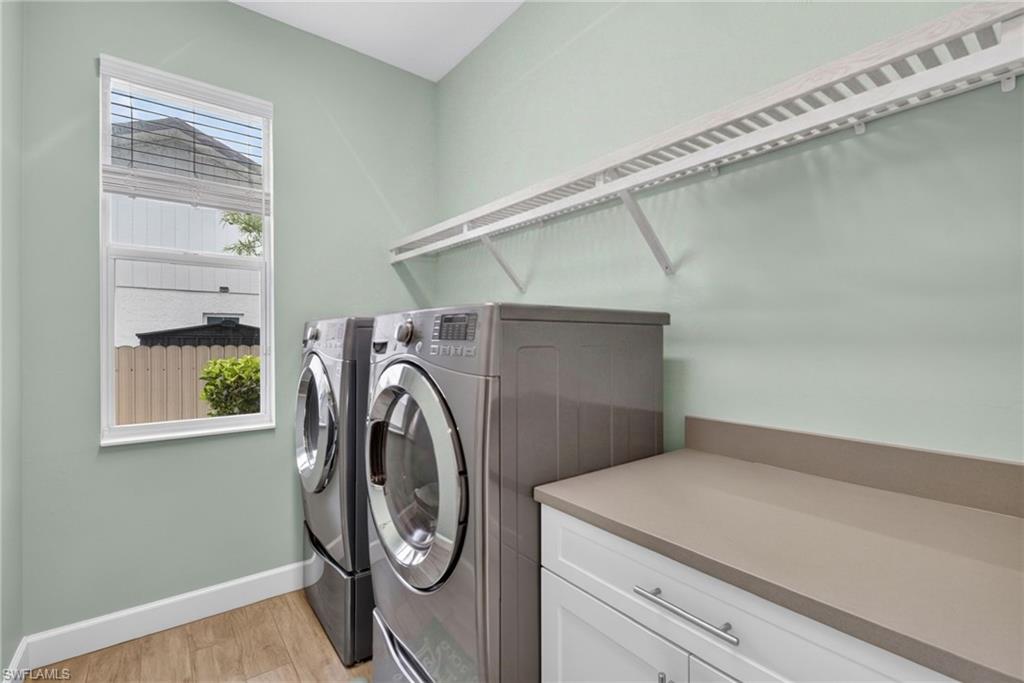 Dedicated laundry space featuring wood-finish flooring, a tall window, a substantial countertop, and white cabinetry