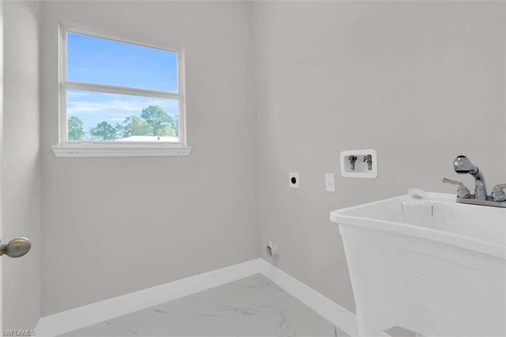 Utility room featuring a single window, a white utility sink, chrome faucet, and tile flooring