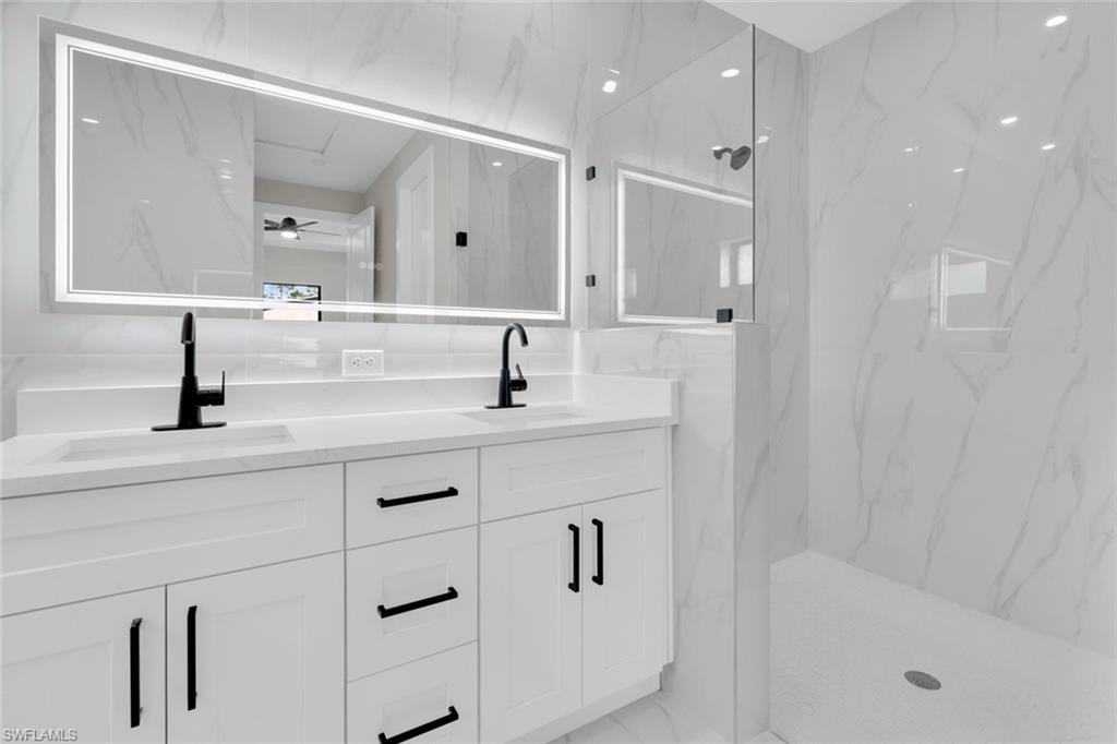 Contemporary bathroom featuring a double vanity with integrated sinks, matte black hardware, an illuminated mirror, and a glass-enclosed shower with a built-in bench