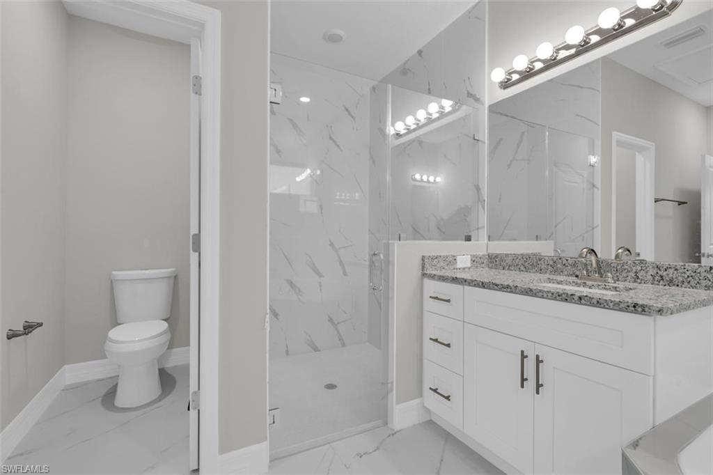 Bathroom featuring a clear glass shower enclosure with marble-patterned tile, a white vanity with a speckled countertop, an undermount sink, and a wall-mounted light fixture above a large mirror