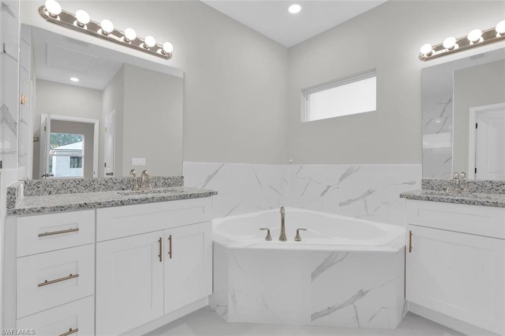 Corner soaking tub with a tiled surround, flanked by twin vanity cabinets featuring granite countertops and undermount sinks