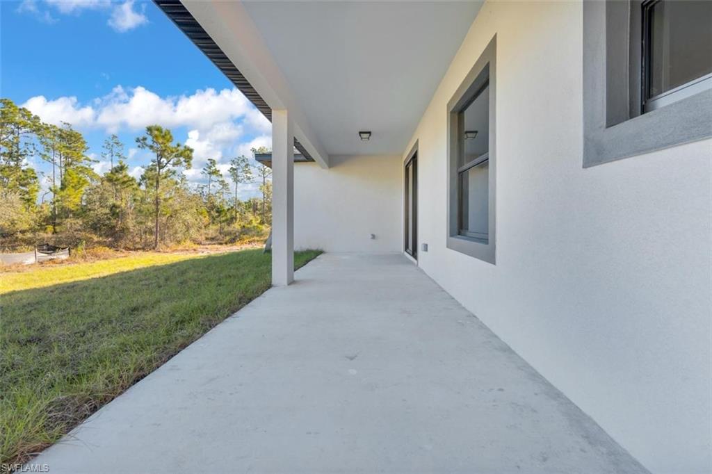 Covered concrete patio with white stucco exterior, framed by dark gray window trim and a glass sliding door