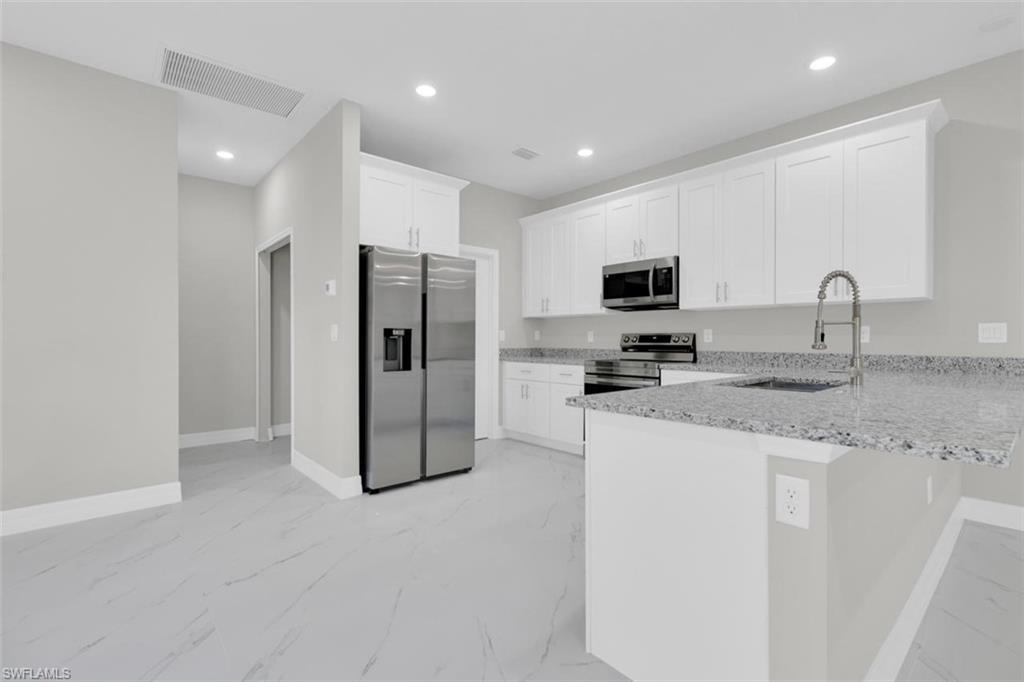 Kitchen featuring white shaker-style cabinetry, stainless steel appliances, granite countertops, and light gray tile flooring