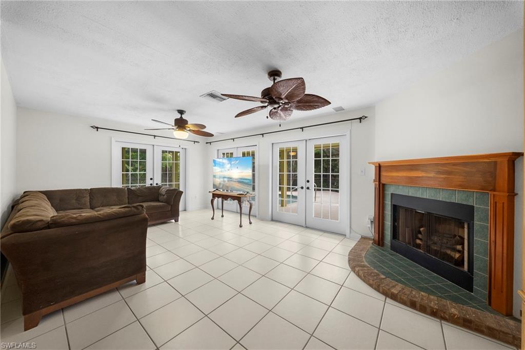 Living area featuring white tile flooring, a wood-finish mantel with green tile surround, and two sets of double French doors