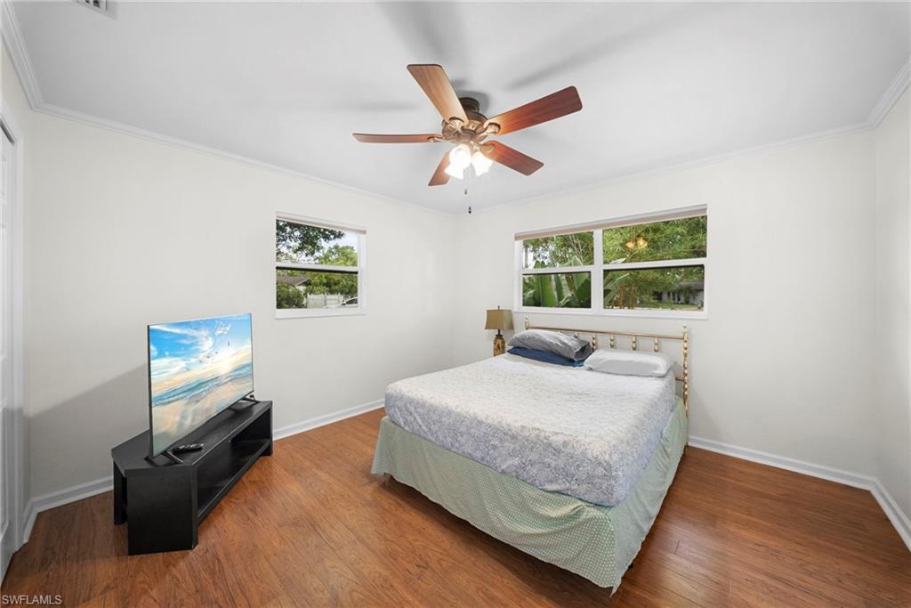 Bedroom featuring wood-finish flooring, two windows, crown molding, and a ceiling fan with integrated lighting