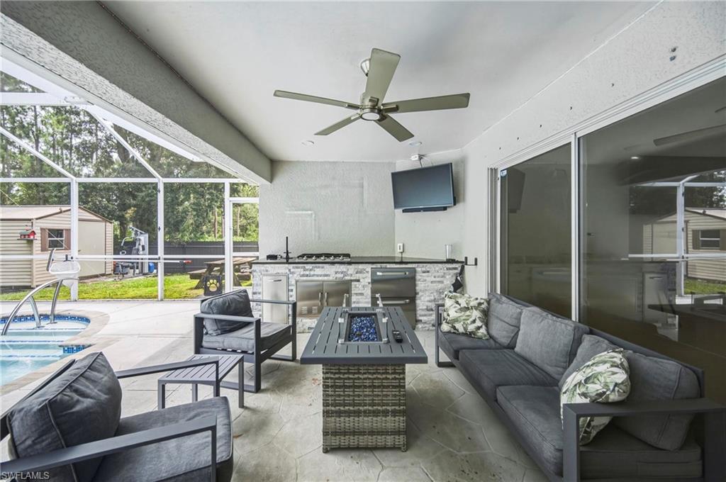 Screened patio featuring a built-in outdoor kitchen with stone veneer and stainless steel appliances, a ceiling fan, and sliding glass doors