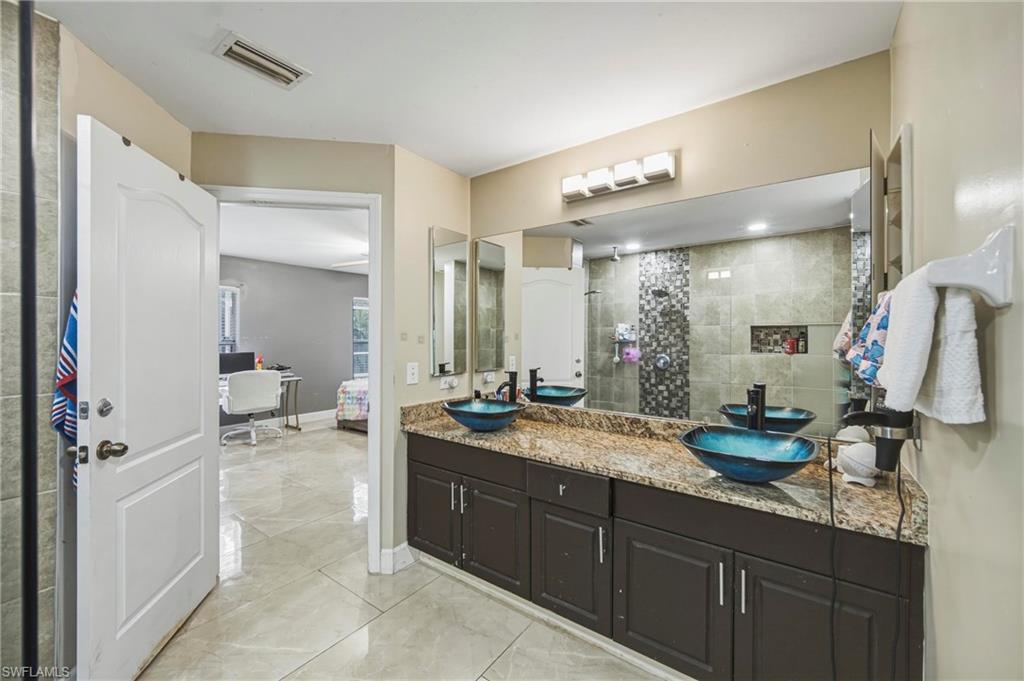 Bathroom featuring a dual vanity with vessel sinks, a granite-finish countertop, dark wood cabinetry, and a large wall-mounted mirror