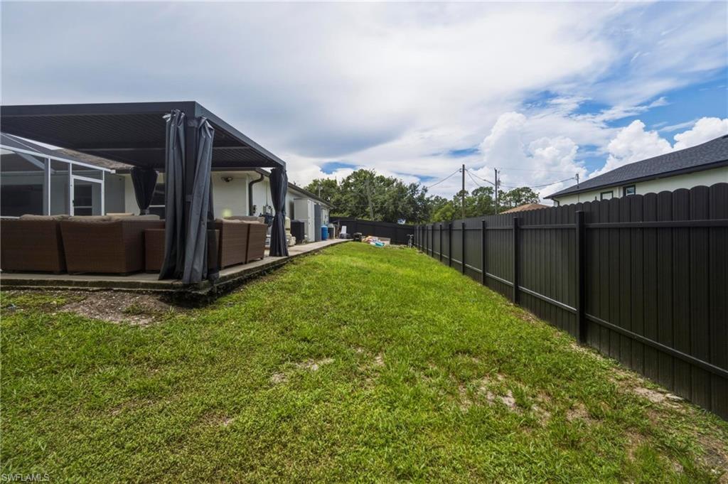 Expansive backyard featuring a lush lawn, solid privacy fencing, and a covered patio area