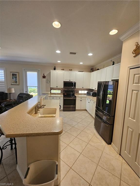 Kitchen featuring stainless steel appliances, ornamental molding, white cabinetry, an island with sink, and recessed lighting