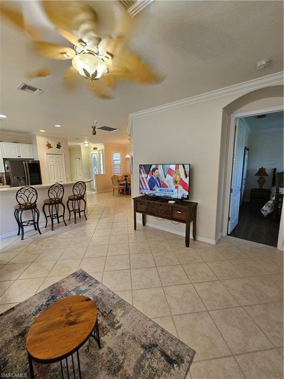 Living area featuring crown molding, a ceiling fan, light tile patterned floors, and arched walkways
