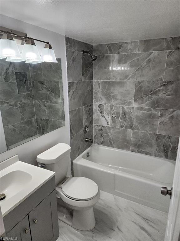 Bathroom featuring a bathtub with a shower, gray marble-patterned tile surround, and a built-in shower niche