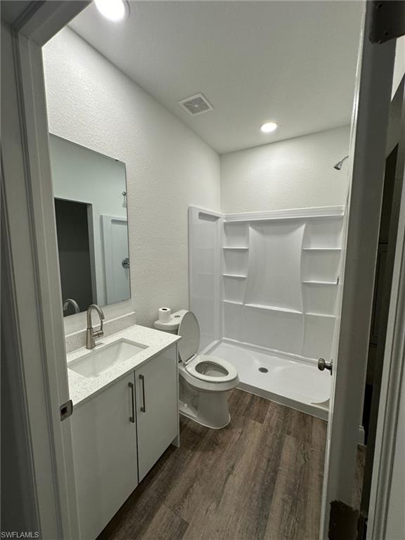 Bathroom featuring wood-finish flooring, a white vanity with a light-colored countertop and integrated sink, a brushed nickel faucet, a frameless mirror, and a stand-up shower with a white surround