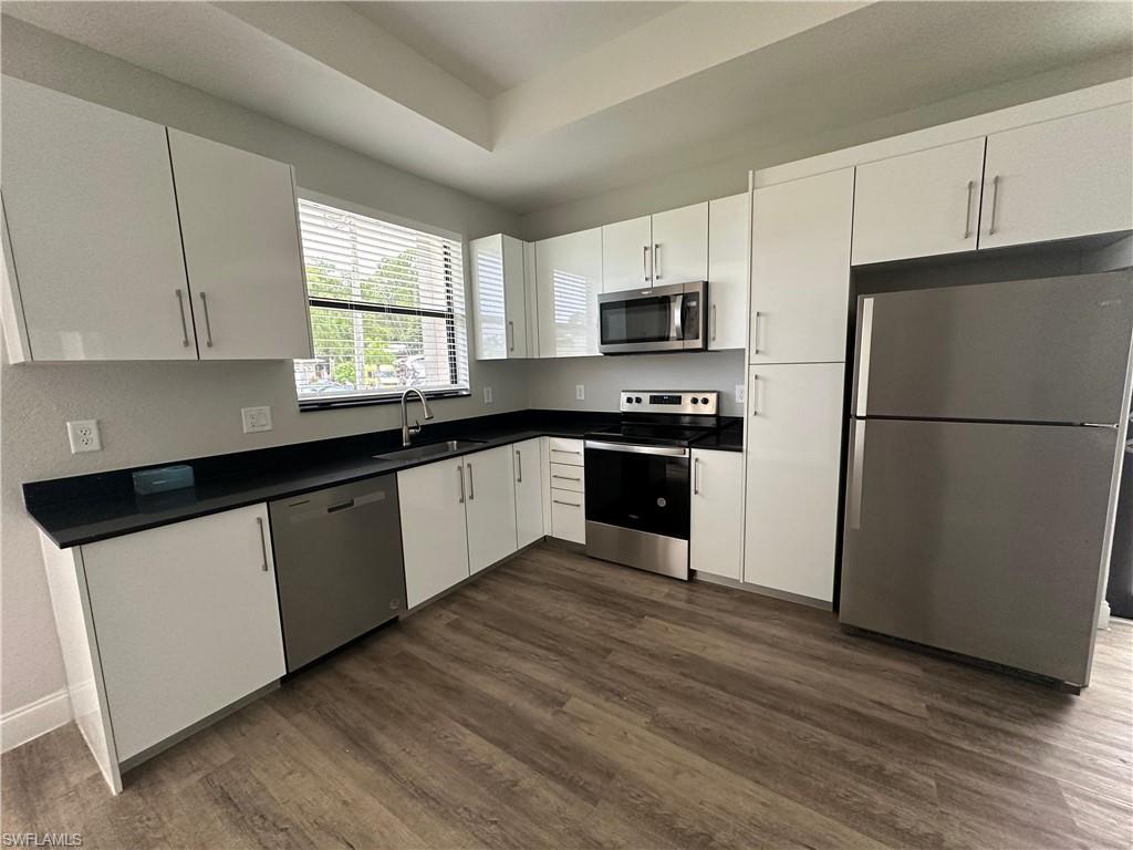 Modern kitchen featuring white cabinetry, dark countertops, and wood-finish flooring