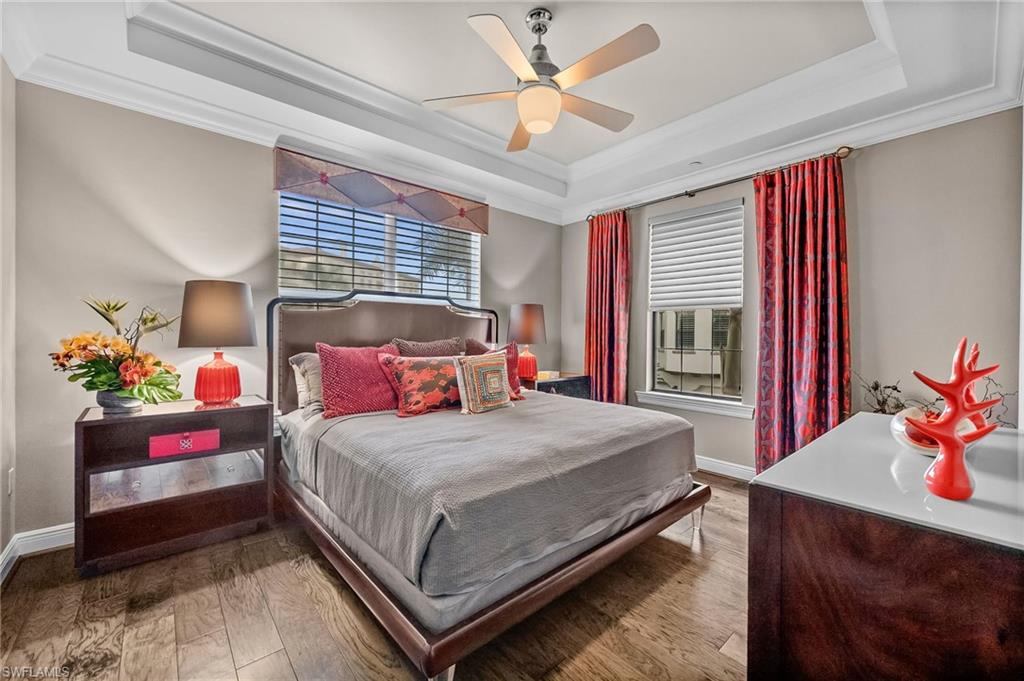 Bedroom with crown molding, a raised ceiling, hardwood / wood-style flooring, multiple windows, and a ceiling fan