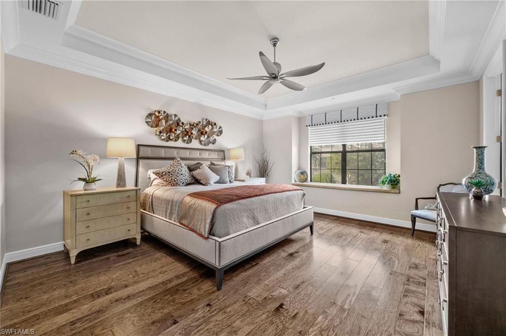 Bedroom with a raised ceiling, crown molding, wood-type flooring, and ceiling fan