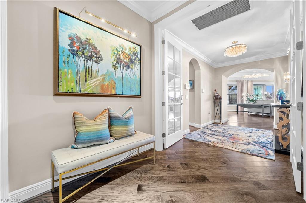 Entrance foyer with arched walkways, crown molding, dark wood-style flooring, and a chandelier