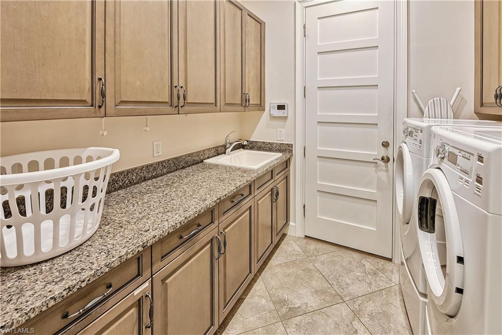 Clothes washing area featuring washing machine and dryer, sink, and cabinets