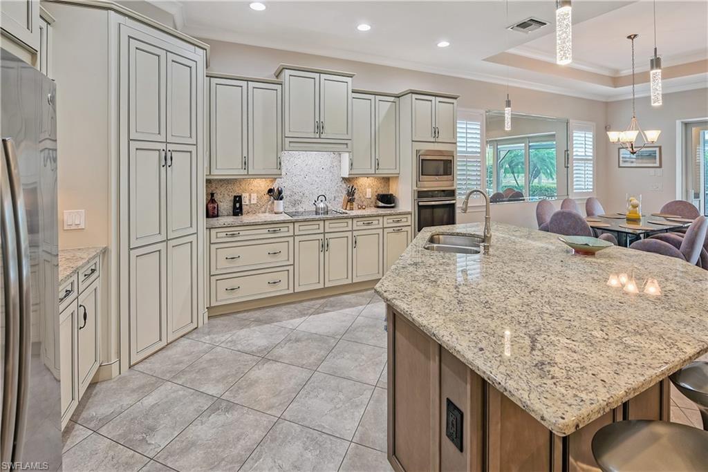 Kitchen featuring stainless steel appliances, decorative light fixtures, a kitchen bar, a center island with sink, and ornamental molding