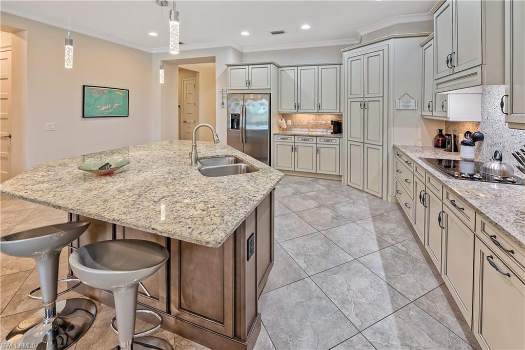 Kitchen featuring decorative backsplash, stainless steel refrigerator with ice dispenser, a center island with sink, and hanging light fixtures