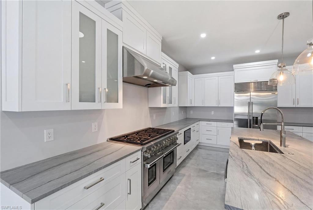 Gourmet kitchen featuring white shaker cabinetry, stainless steel appliances, a six-burner gas range with a matching range hood, and light-toned countertops with distinctive veining