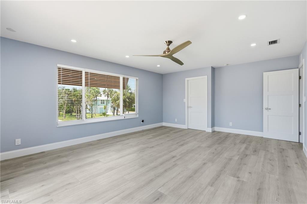 Spacious interior with light wood-finish flooring, light blue walls, recessed lighting, and a modern ceiling fan