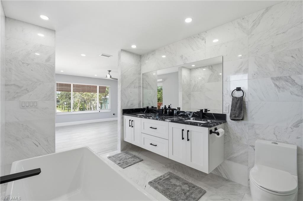 Contemporary bathroom featuring a floating dual vanity with black countertops, a deep soaking tub with a matte black faucet, and a wall-mounted toilet