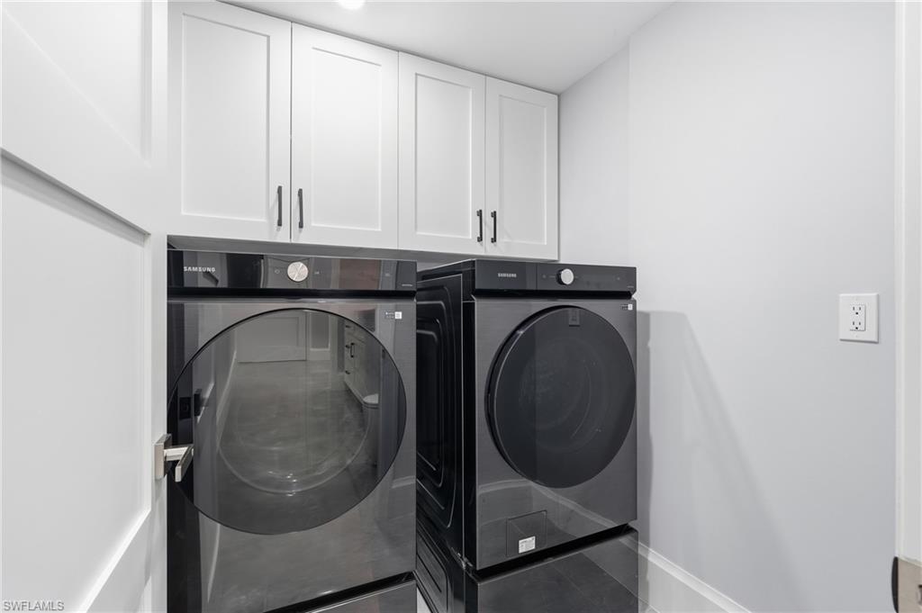 Laundry area featuring white shaker-style cabinetry with matte black hardware, light gray wall paint, and a white baseboard trim