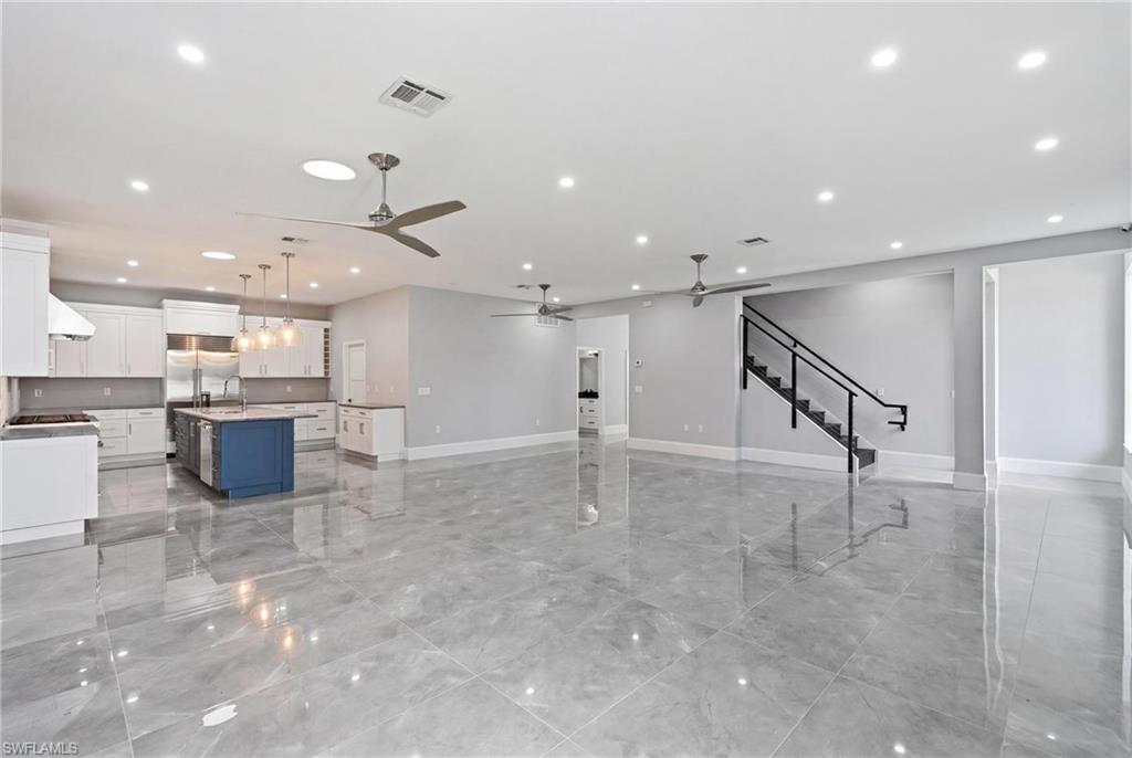 Spacious interior featuring a contemporary kitchen with a blue island, stainless steel appliances, white cabinetry, and pendant lighting