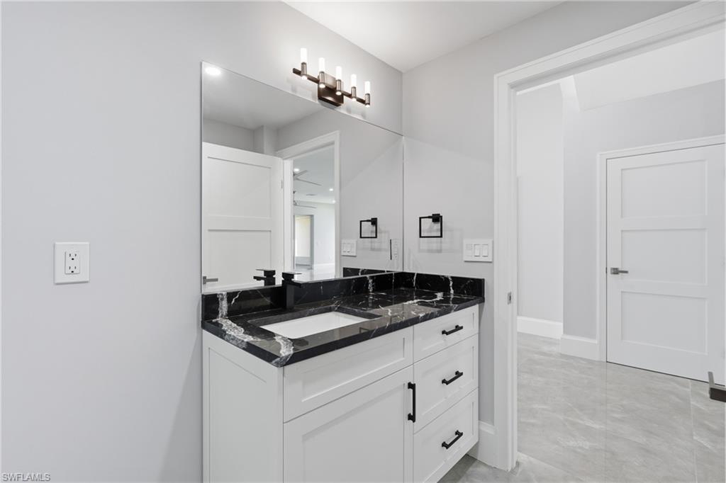 Contemporary bathroom vanity featuring a white shaker-style cabinet, black veined countertop, integrated rectangular sink, and matte black hardware